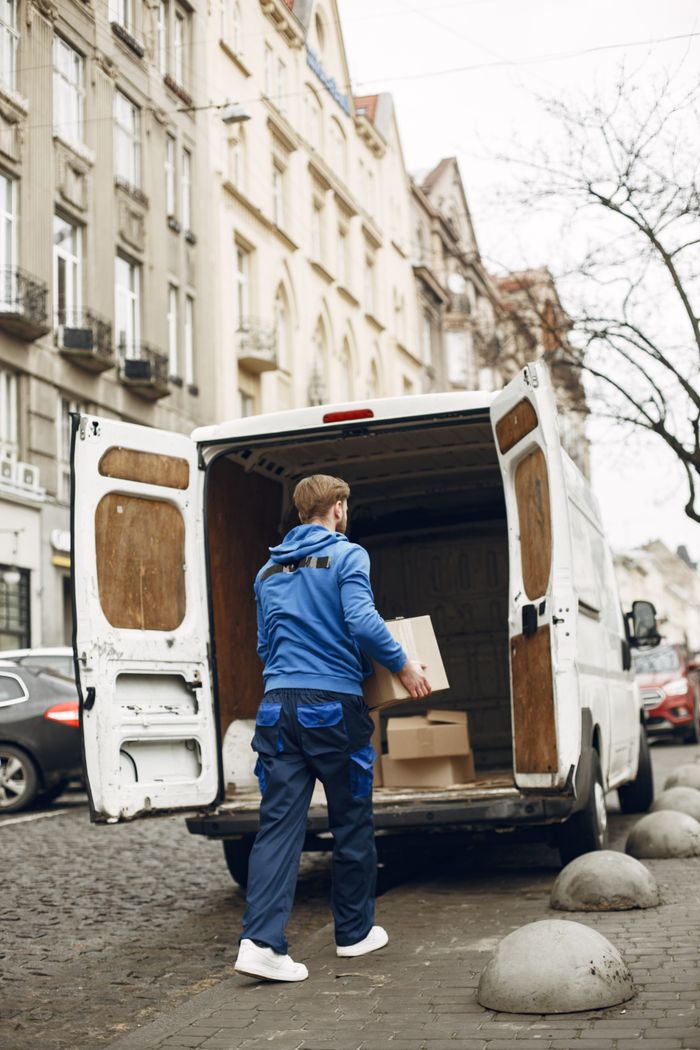 A delivery person loads boxes into a van on a cobblestone street, showcasing urban logistics.